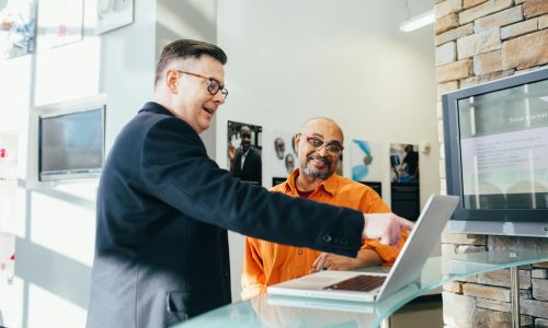 Two businessmen having a lively discussion in a modern office setting, pointing at a laptop screen.