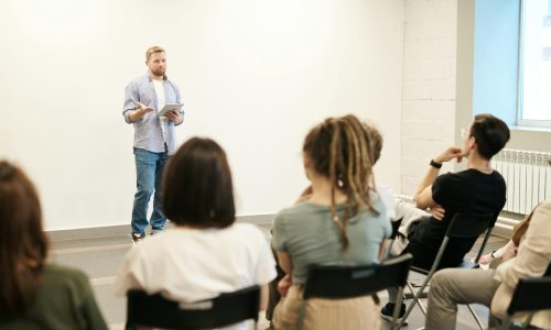 Man presenting with tablet to a small seated audience in a modern indoor setting.