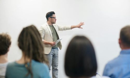 A man in a blazer gives a presentation to a captivated audience in a lecture setting.