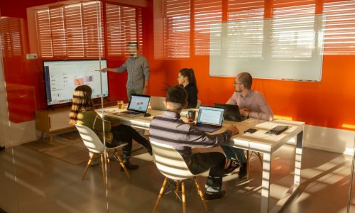 a group of people sitting around a table with laptops
