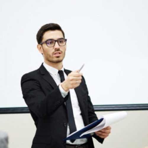 Confident coach pointing at one of listeners while making report at training