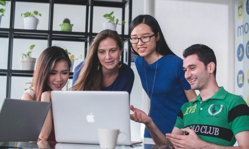 four people watching on white MacBook on top of glass-top table